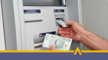 Osoba wypłacająca gotówkę z bankomatu – karta płatnicza i banknot 100 złotych