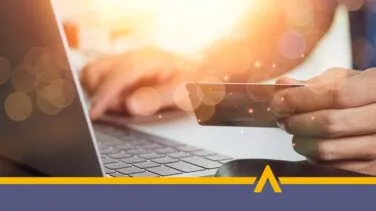 Osoba trzymająca kartę płatniczą przy laptopie podczas płatności online